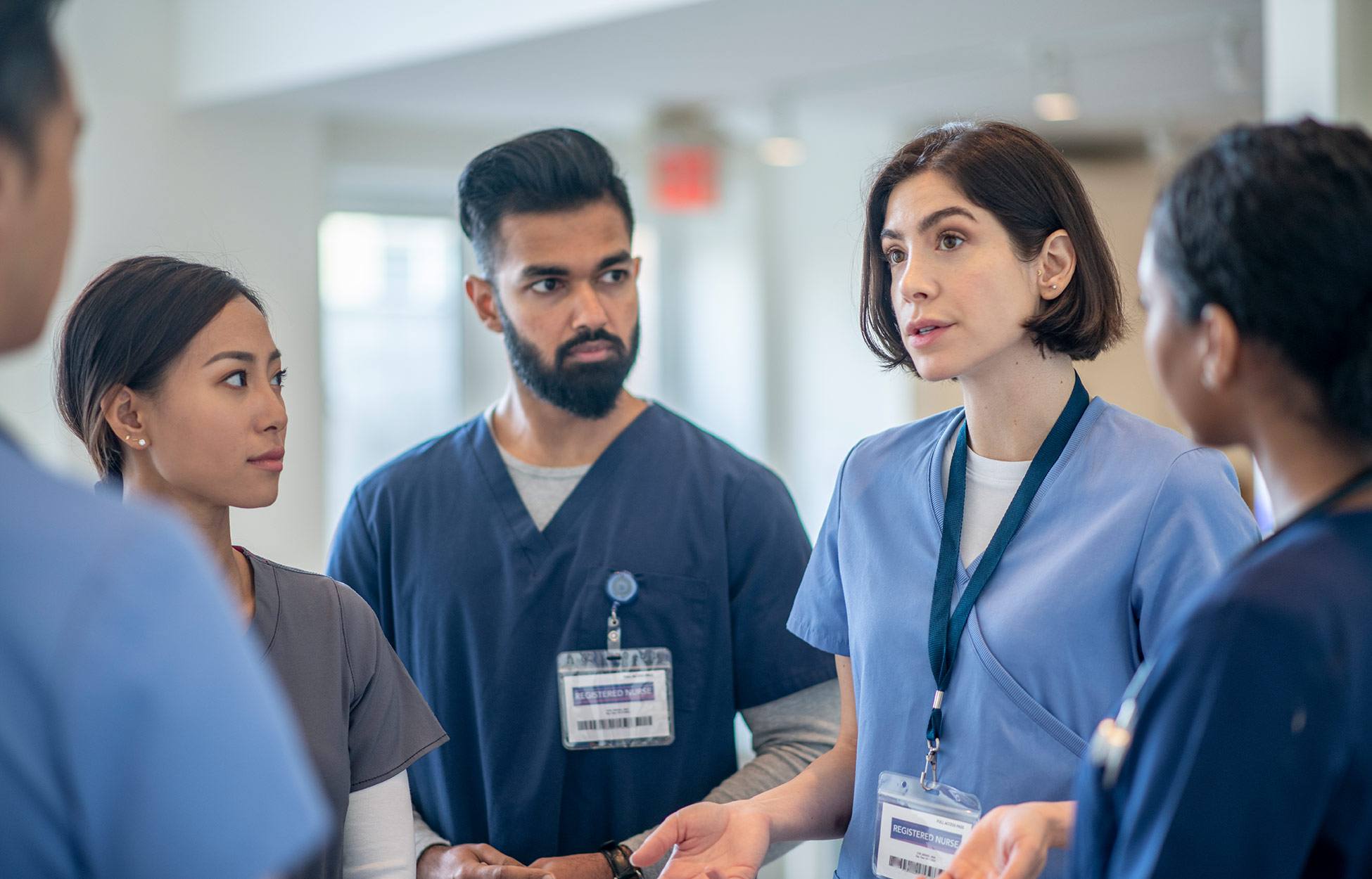 A group of medical professionals in blue scrubs talking in a circle